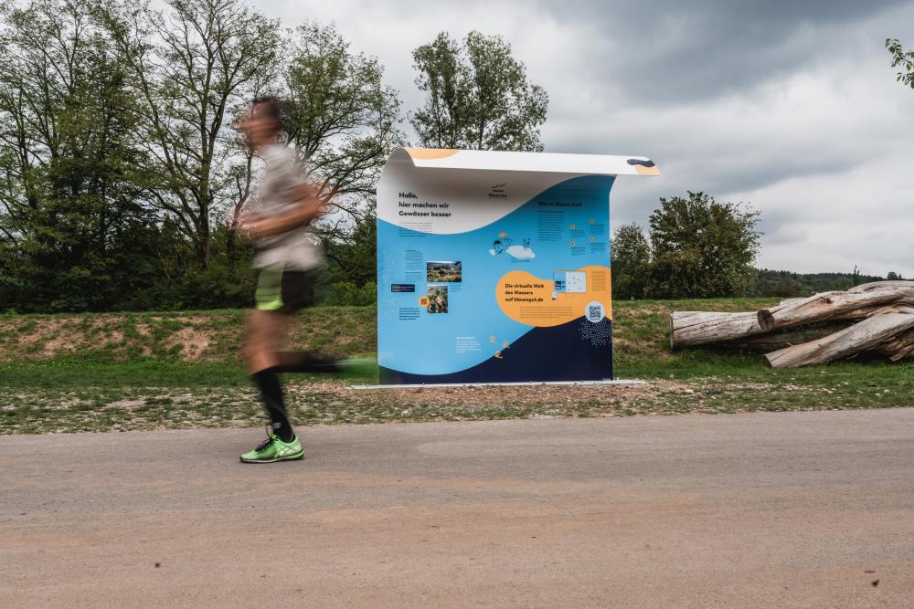 Ein Man joggt an einer Maßnahmen Informationstafel vorbei 