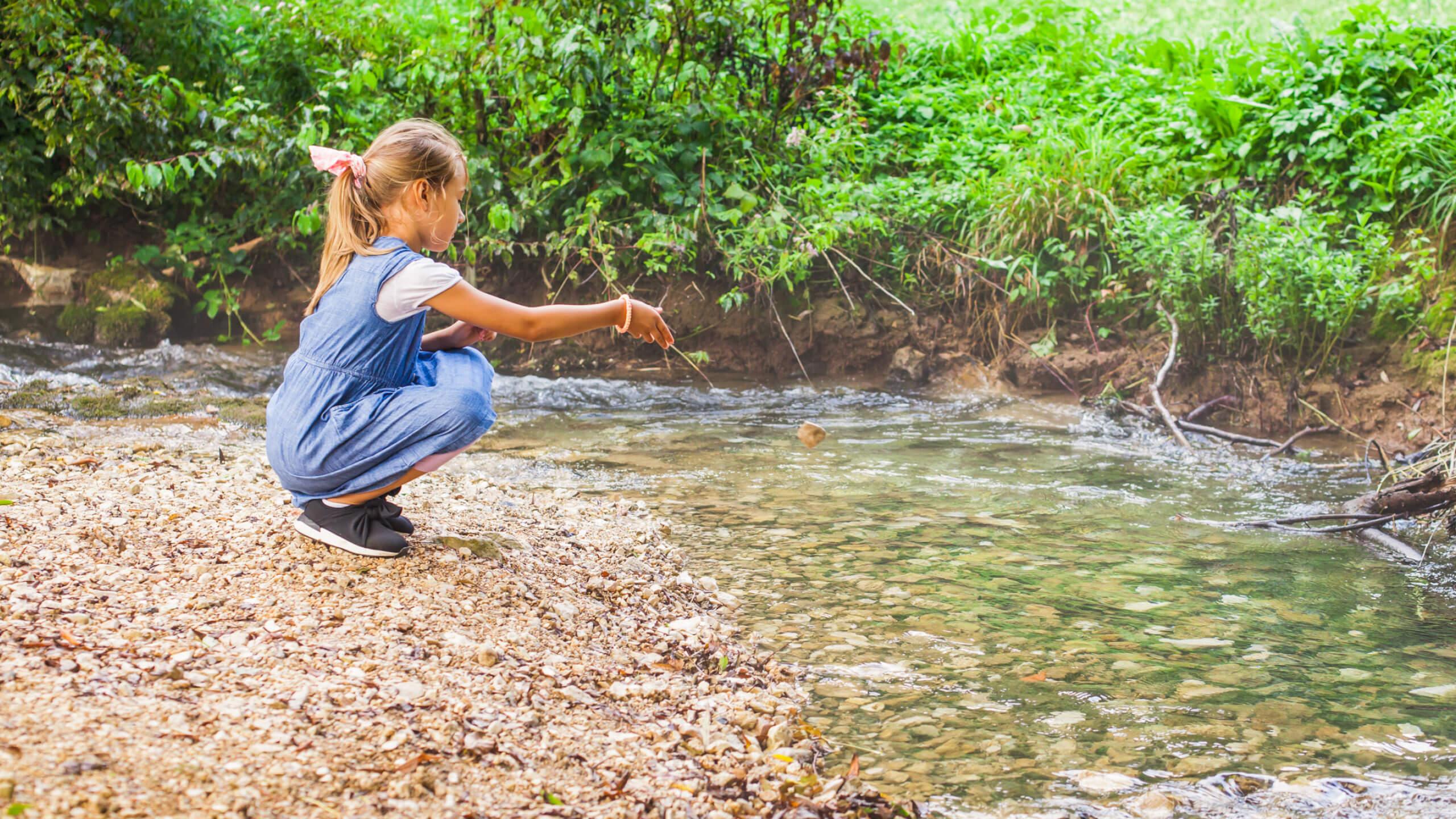 Ein Mädchen spielt am Wasser und mit Steinen, während sie die Natur erkundet und Spaß hat.